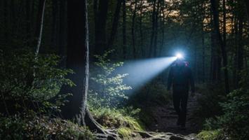 Vandrer med tændt pandelygte på en skovsti i skumringen